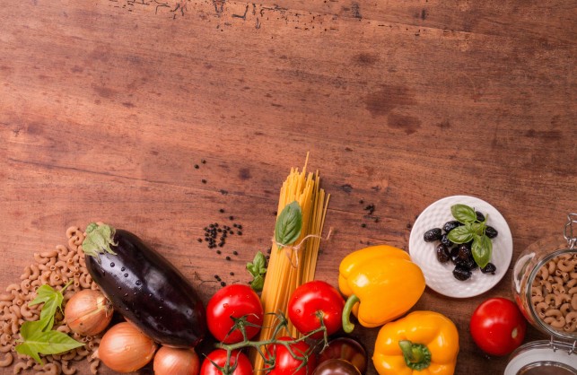 An image of a solid wood, traditional kitchen table which has fresh food laid out on it.